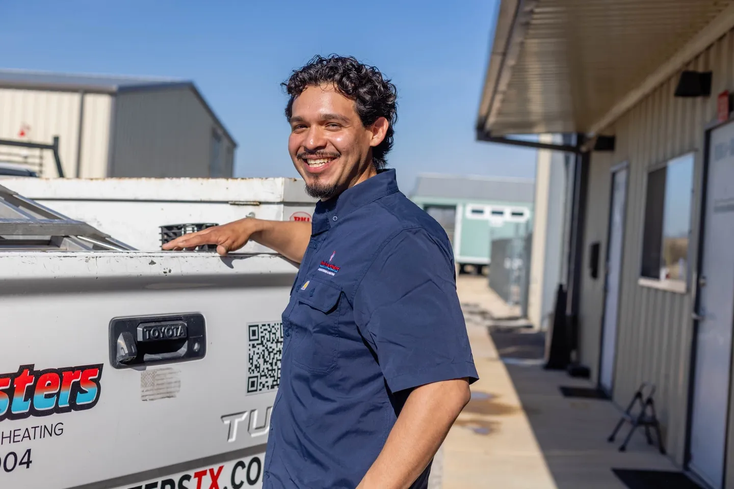 Smiling technician in blue uniform by service truck